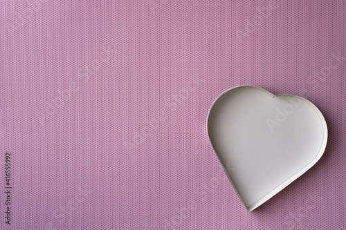 An empty, white heart-shaped box on a pink background with a pattern of small, darker pink dots. 