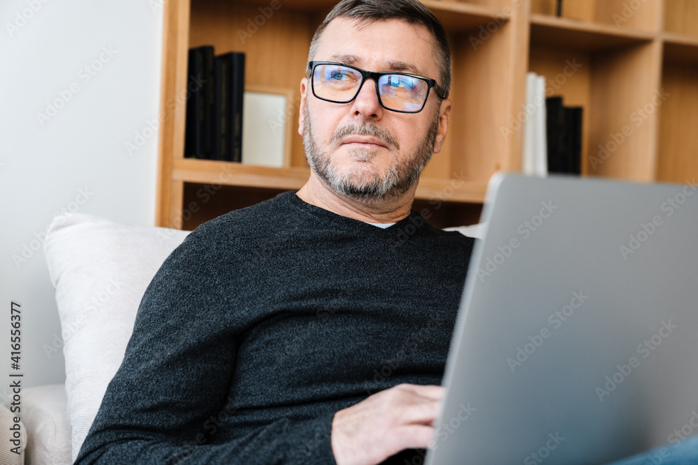 Serious adult unshaven man working with laptop while sitting at home Serious adult unshaven man working with laptop while sitting at home
