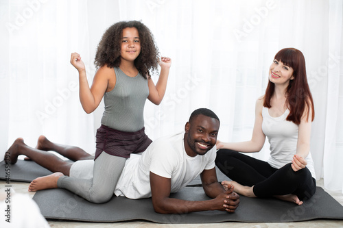 Curly teen mixed race girl doing gymnastic exercise in room with her parents