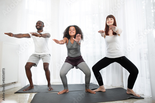 Happy active multiracial family doing squats on the mat at home