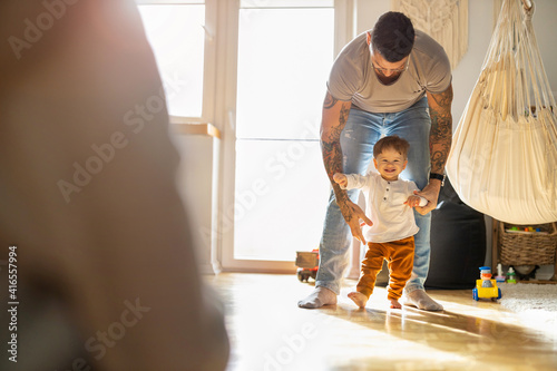 Bilde på lerret Happy father helping little son walking in living room