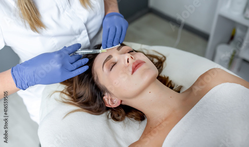 Girl beautician makes injections on the lips and face of a beautiful woman in a cosmetic wedge. Cosmetology concept.