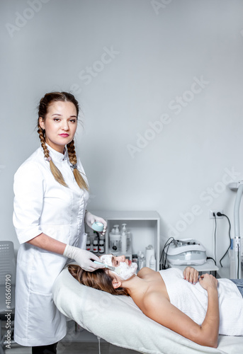 The imposition of a cosmetic mask on the face. A cosmetologist-dermatologist in a cosmetic clinic. photo