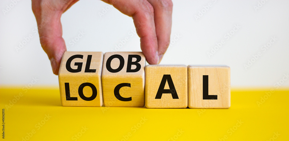 Local or global symbol. Businessman turns wooden cubes and changes the word 'local' to 'global'. Beautiful yellow table, white background. Business and local or global concept. Copy space. - obrazy, fototapety, plakaty 