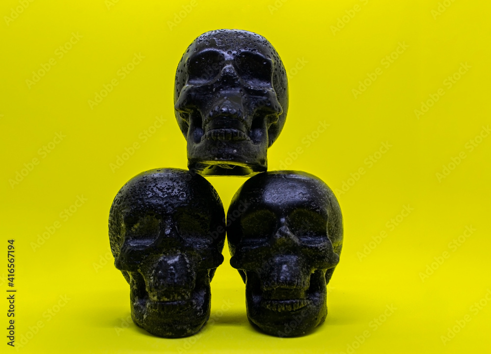 Three black wax skulls on a yellow background.