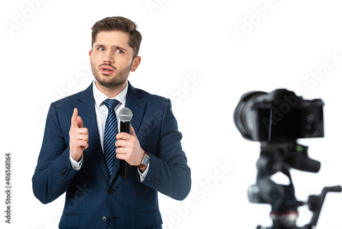 serious news presenter with microphone pointing with finger near digital camera on blurred foreground isolated on white photo