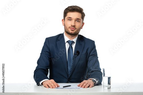 news anchor looking at camera while sitting at workplace near papers and glass of water isolated on white photo