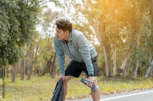 Tired man runner is resting after morning cardio outdoors with towel and water bottle. © C_Production