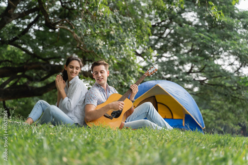 Picnic and Camping time. Young couple having fun with guitar on picnic and Camping in the park. Love and tenderness, Romantic man playing guitar to his girlfriend, lifestyle concept