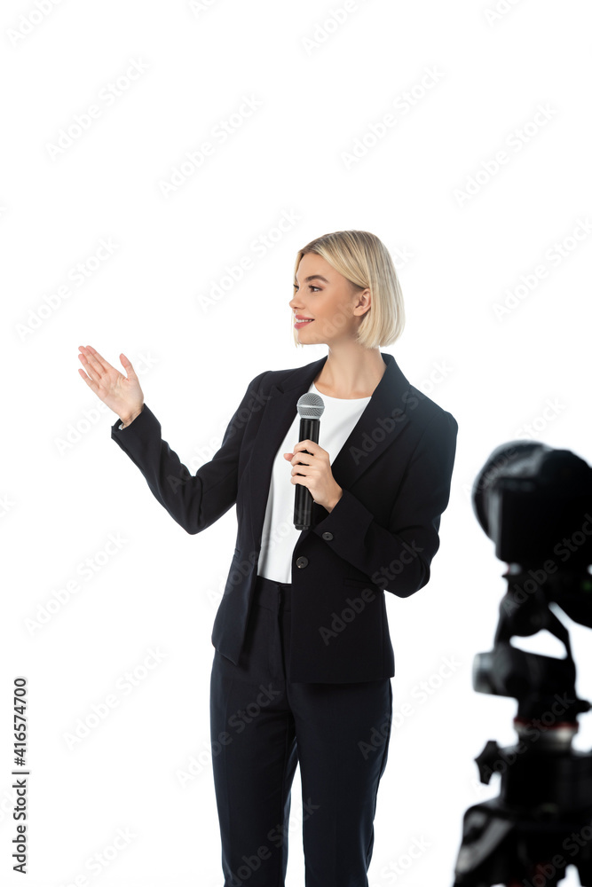 young smiling newscaster with microphone pointing with hand near digital camera on blurred foreground isolated on white young smiling newscaster with microphone pointing with hand near digital camera on blurred foreground isolated on white