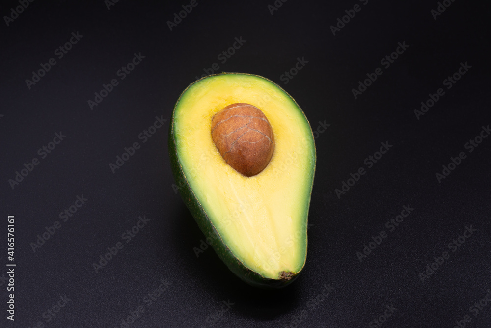 Half an avocado with a bone on a black background