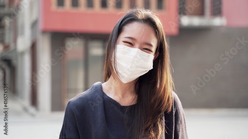 Beautiful asian woman wearing protective medical mask and standing on the street. Safe and Happy Woman Practicing Social Distancing, Quarantine. Health care and medical concept. Close up portrait . 4k