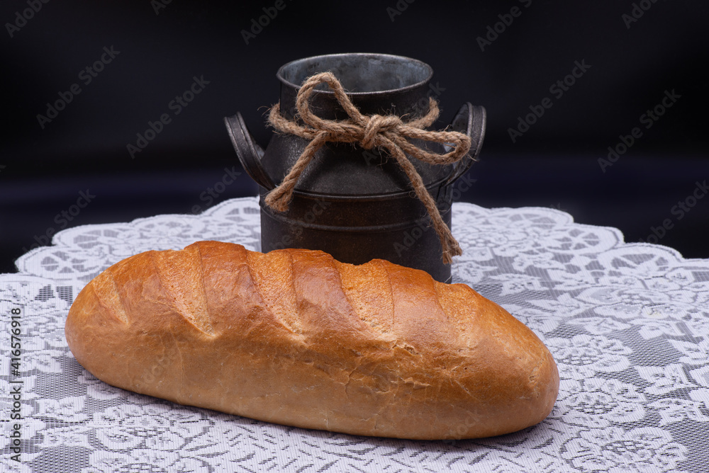 Composition of white bread and old jug on white tablecloth on black background