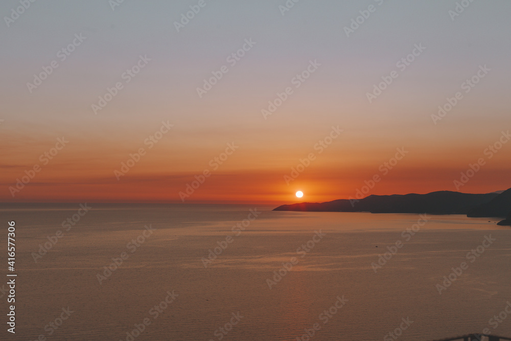 Sun going down behind the hills and sea. Romantic sunrise or sunset over sea with hills in background