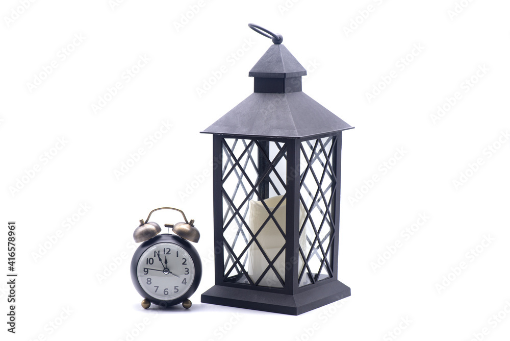 Glass lamp with a candle inside and retro alarm clockon a white background