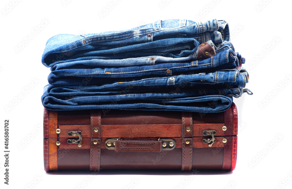 Stack of blue jeans on a brown retro suitcase on white background