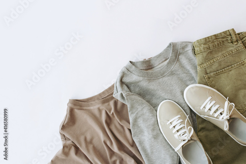 women's cappuccino-colored t-shirt, gray sweatshirt, green jeans and beige sneakers are laid out in the lower right corner, top view