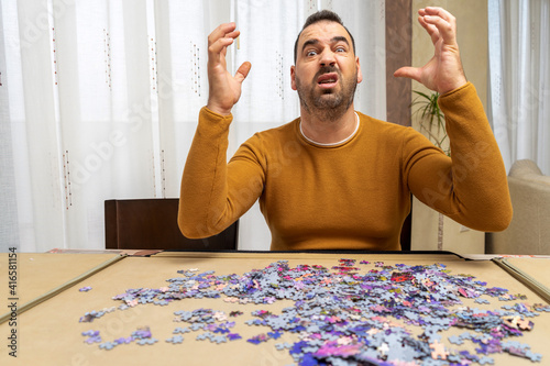 Bearded man screaming with raised hands desperate for the complexity of assembling a puzzle in the living room