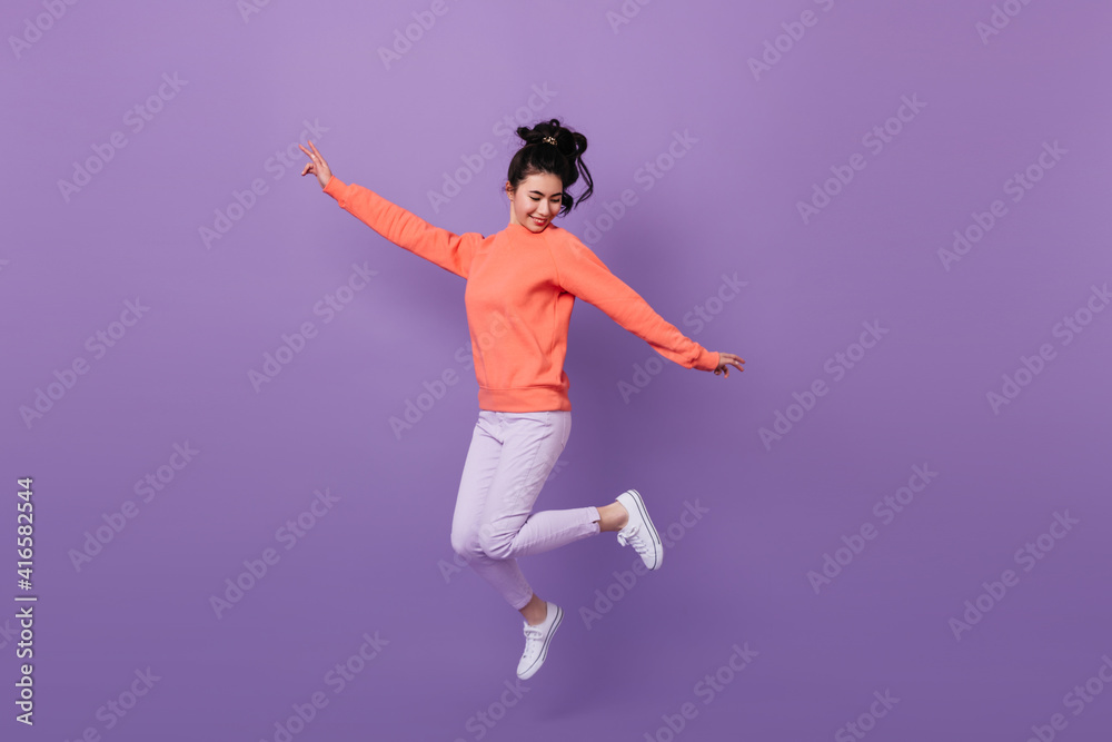 Carefree pretty asian girl jumping with smile. Studio shot of funny korean woman dancing on purple background.