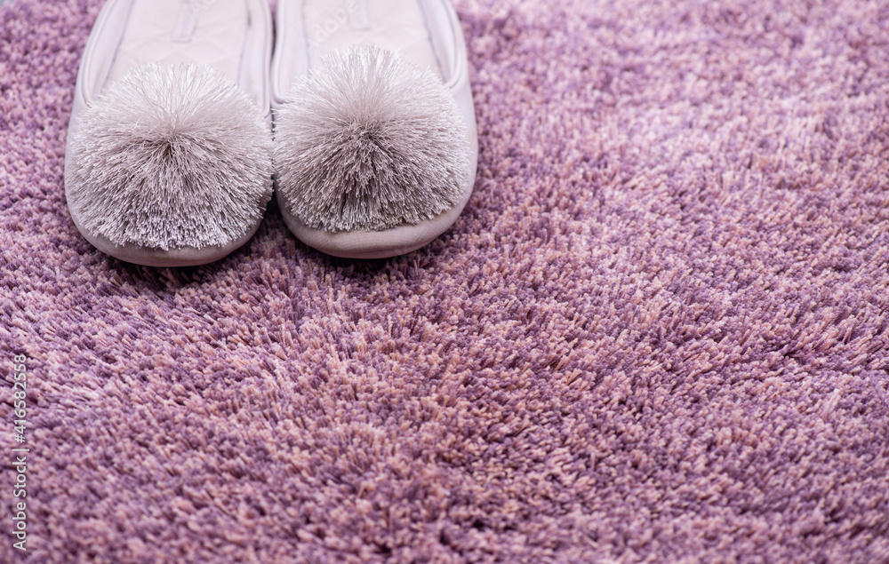 Women's gray slippers with a fluffy pompom on a fluffy bath mat