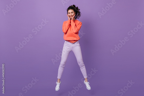 Blithesome asian young woman jumping and looking at camera. Stunning japanese girl dancing on purple background.