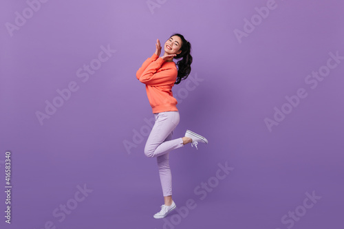 Refined asian woman standing on one leg. Full length view of blissful chinese girl dancing on purple background.