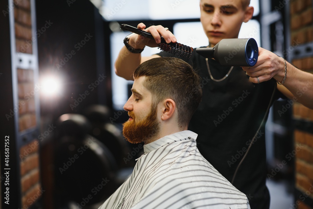 Young handsome barber making haircut of attractive bearded man in barbershop Young handsome barber making haircut of attractive bearded man in barbershop