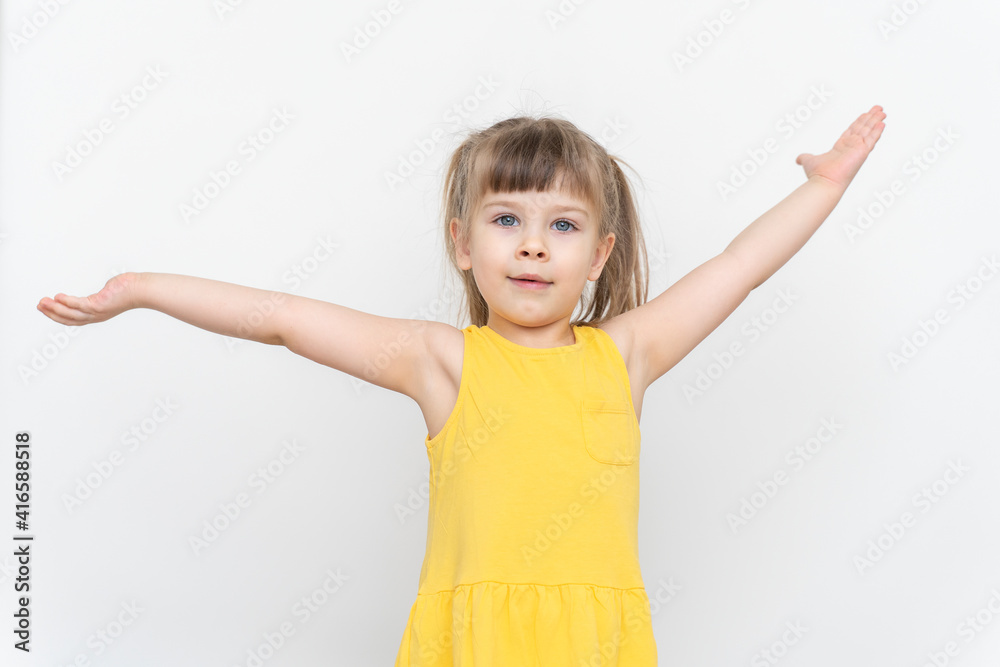 cheerful caucasian child girl in a yellow dress on a gray background, hands to the sides cheerful caucasian child girl in a yellow dress on a gray background, hands to the sides