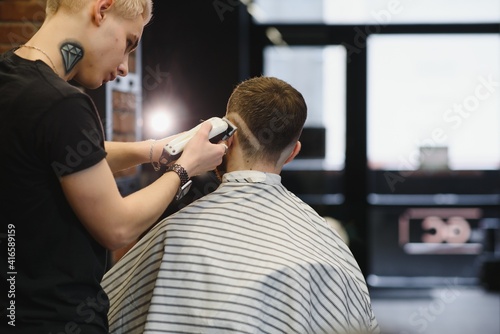 Making haircut look perfect. Young bearded man getting haircut by hairdresser while sitting in chair at barbershop