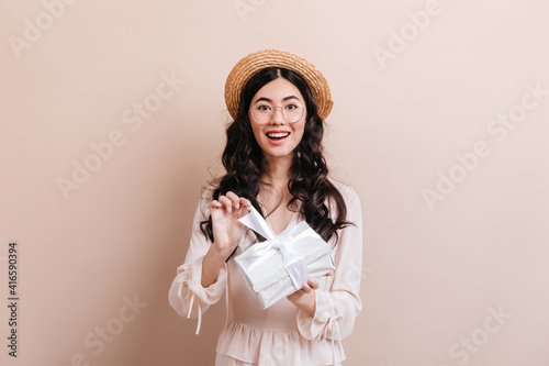 Gorgeous asian girl opening birthday present. Front view of glad korean woman with gift.