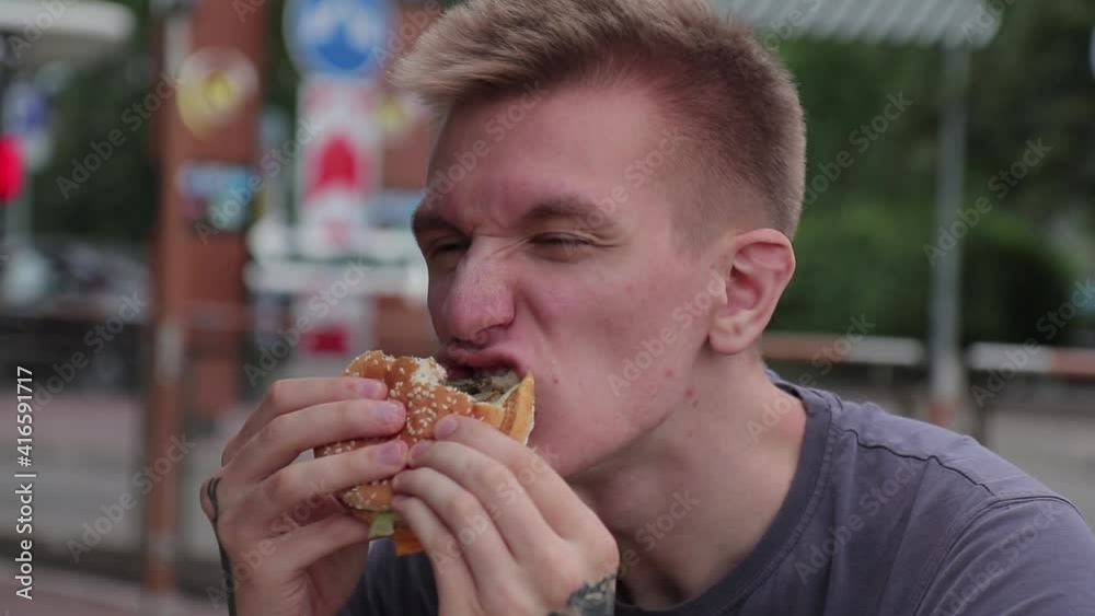 hungry man appetizingly chews a burger after workout in the street hungry man appetizingly chews a burger after workout in the street