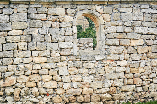 stone wall of an ancient building with a semicircular window  beyond which other ruins are visible