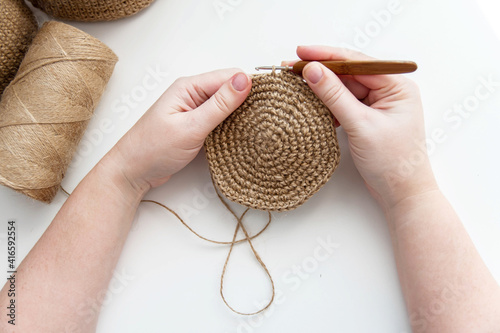 Women's hands knit a circle crochet with a wooden jute hook.