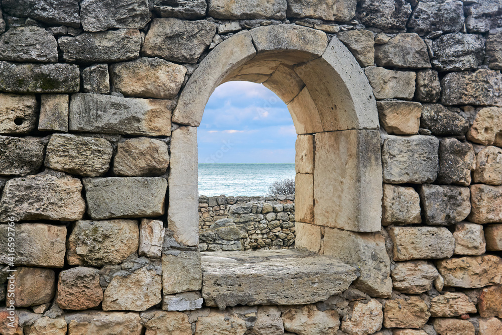 window opening in the ruins of an antique wall, behind which you can see the sea
