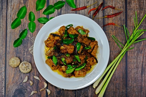 Stir fired pork rips with chilli, lemongrass and kaffir lime leaves surrounded by key ingredients on wooden table. Authentic Thai food.
