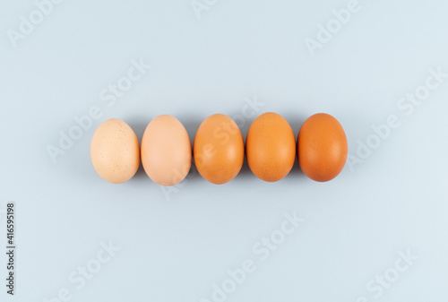 Eggs of different shades of color in a row on a blue background. Copy space.