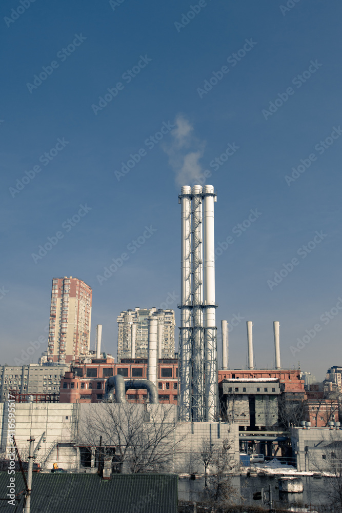 Combined heat and power plant. Smoke from the chimneys of a large factory. Large steam pipes of a working plant