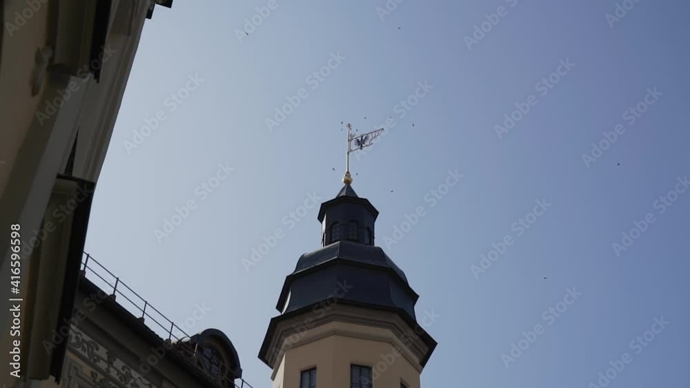 View of the castle tower with weather vane with image of eagle near which many swallow birds fly. View of the castle tower with weather vane with image of eagle near which many swallow birds fly.