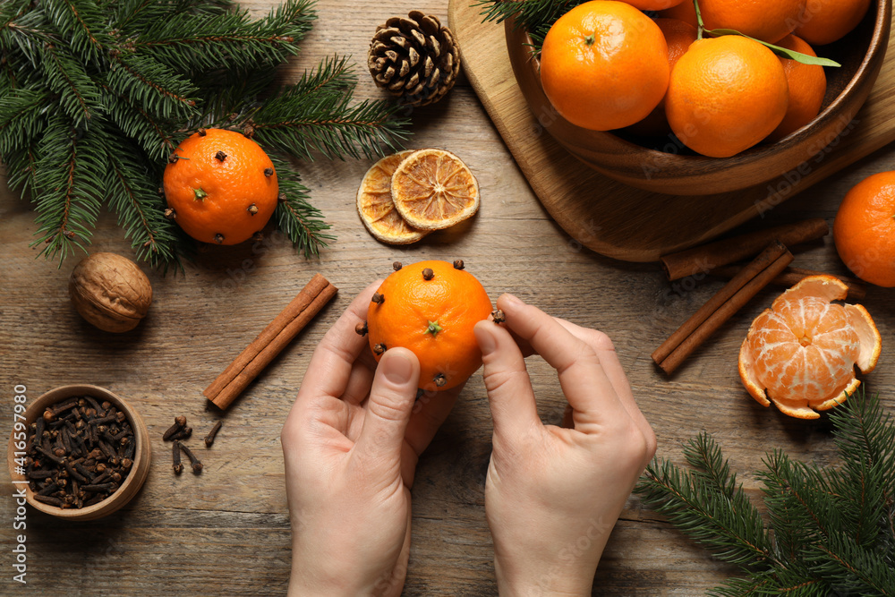 Woman decorating fresh tangerine with cloves at wooden table, top view. Christmas atmosphere Woman decorating fresh tangerine with cloves at wooden table, top view. Christmas atmosphere