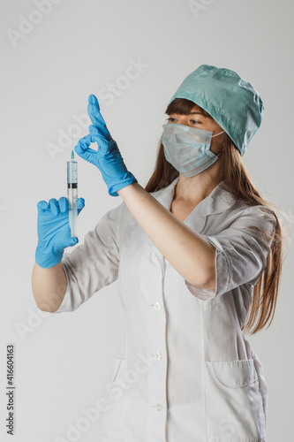 Medicine, vaccination and healthcare concept - female doctor or scientist in mask with syringe. Portrait of a brunette in a blue surgical suitin medical gloves, squeezing a medicine from a syringe photo