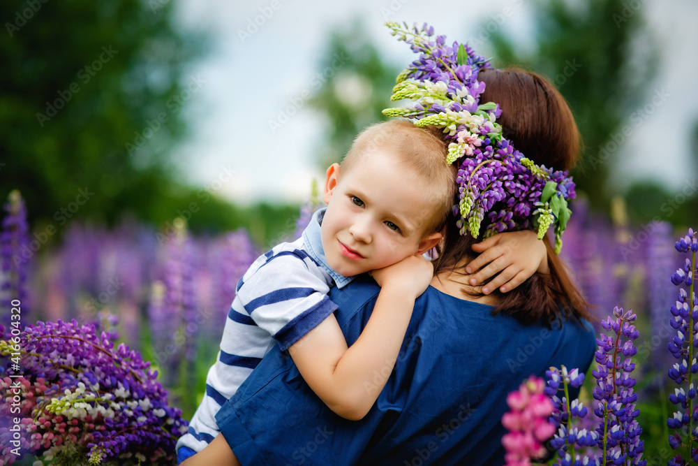 A mother holds her son in her arms in a blooming field of lilac lupine flowers.