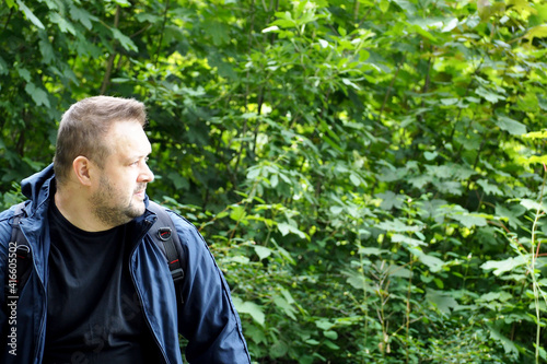 a man in a dark blue jacket sits against a background of green foliage on a summer day in a forest in Europe