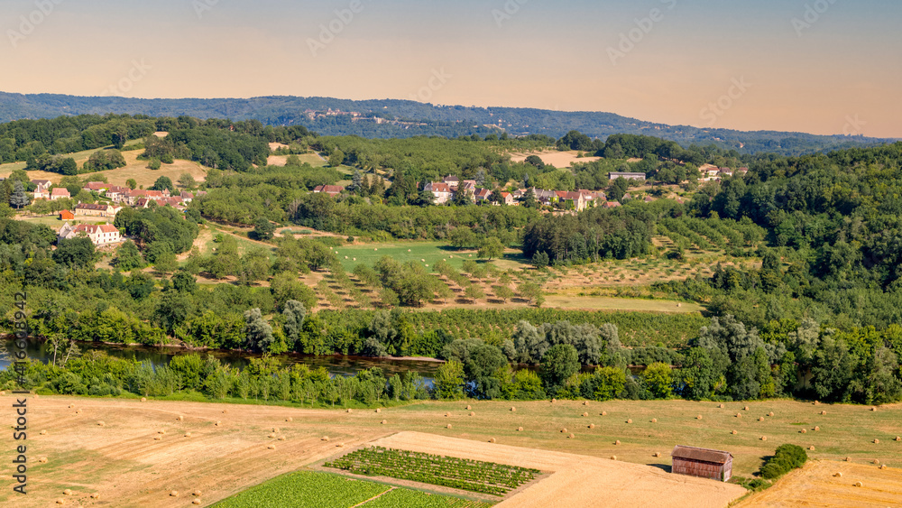 Agricultural landscape in France. Panoramic view of the harvest fields with the round hay bales, green hills and a village in the background.