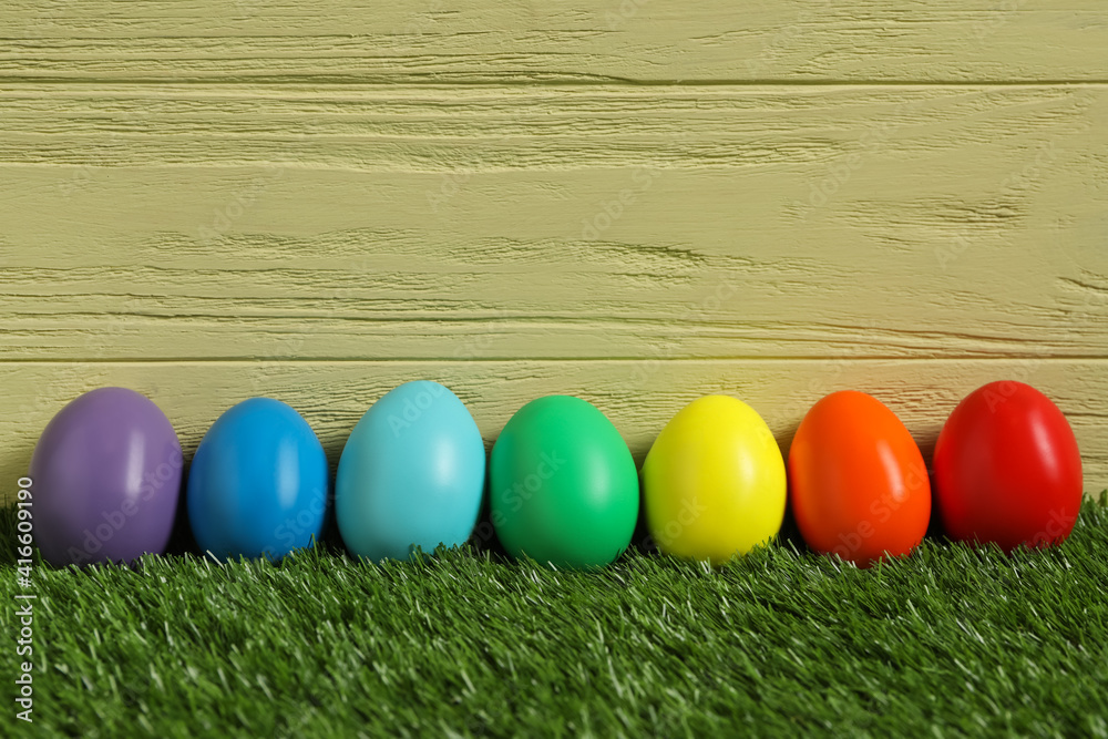 Bright Easter eggs on green grass against yellow wooden background