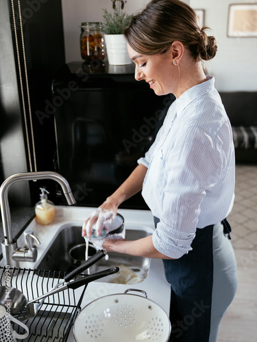Beautiful woman washing dishes at the kitchen sink. Young woman in the kitchen..