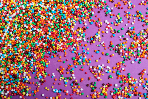 Colorful sprinkles on purple background, flat lay. Confectionery decor