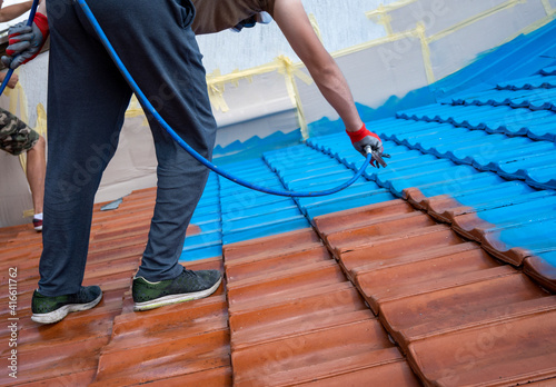 Professional covering old roof tiles with protective layer. He is using high pressure equipment. Before and after, blue and red terracotta. Work at height.