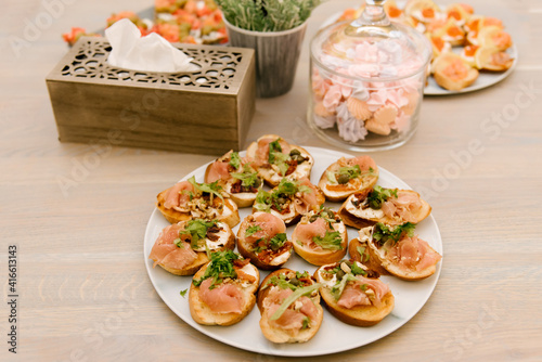 Delicious spicy tomato Italian snacks, or bruschetta, on slices of toasted baguette, decorated with basil, red fish, ham on a wooden board