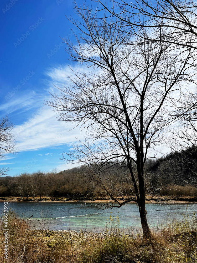 River shoals in winter with dramatic clouds in a blue sky and large tree in the foreground River shoals in winter with dramatic clouds in a blue sky and large tree in the foreground