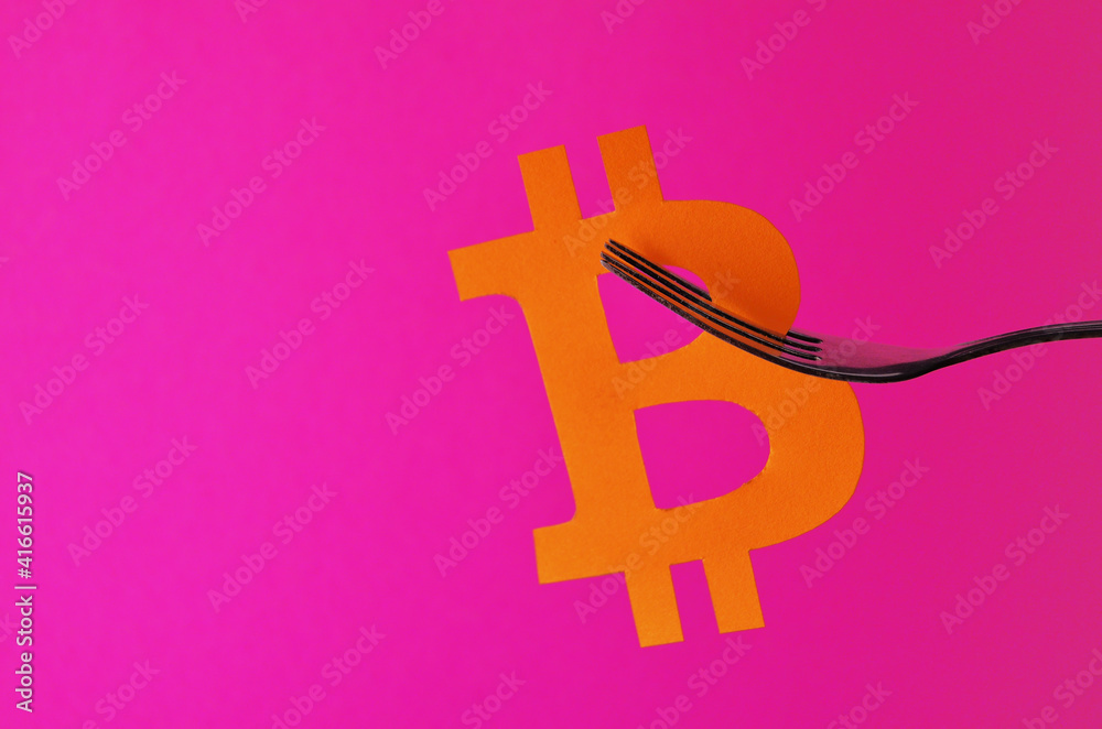 Fototapeta premium The orange bitcoin sign is hung on a fork on a pink background with a copy space. Conceptual collage about cryptocurrency in the style of minimalism. High quality photo